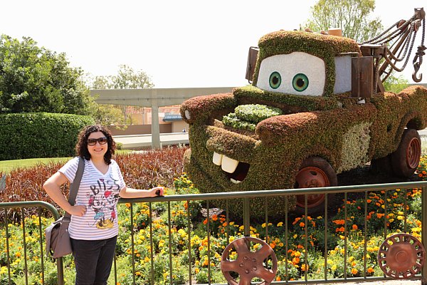 A woman posing next to a topiary that looks like Mater from Cars