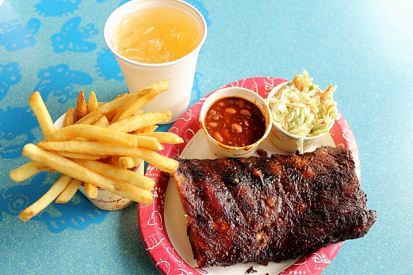 overhead view of ribs, baked beans, coleslaw, french fries, and a drink on a blue table