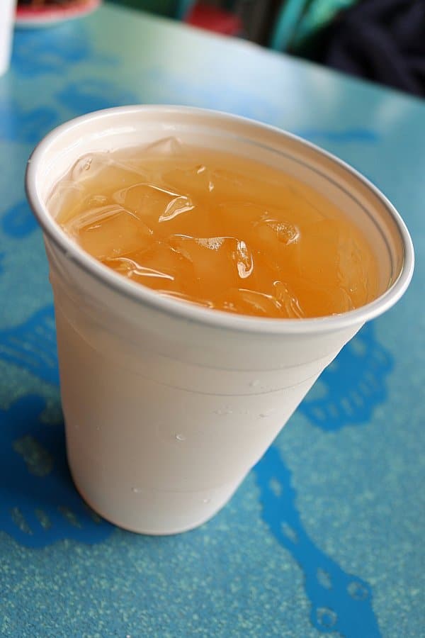 An orange drink with ice in a white plastic cup