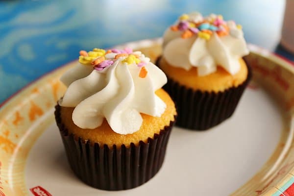 A closeup of two yellow cupcakes with white frosting on a paper plate