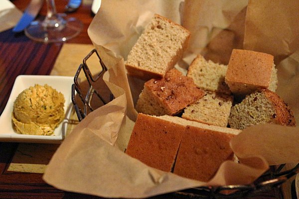 A basket of bread next to a scoop of herbed butter in a white dish