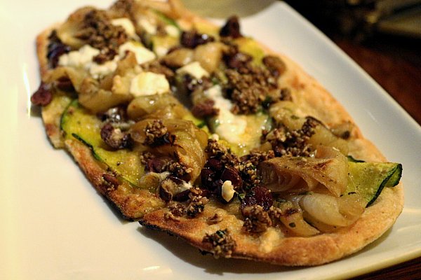 A flatbread with cheese and vegetables on a white plate