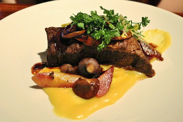 A plate of short ribs with a creamy orange sauce, vegetables and herbs on top