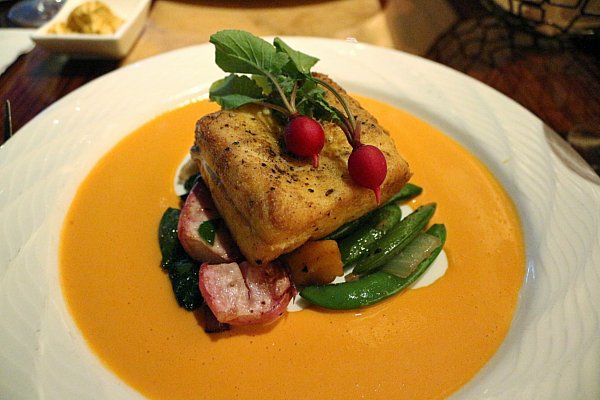 A filet of fish served over colorful vegetables and a bright orange sauce
