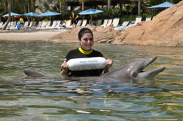 a woman holding a white buoy and posing with a dolphin in the water