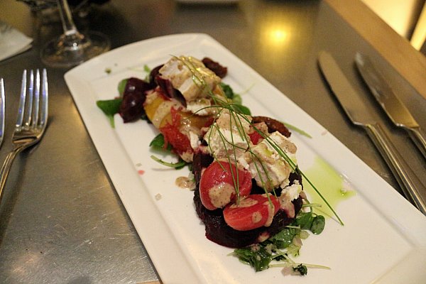 a rectangular white plate with beets and herbs drizzled with dressing