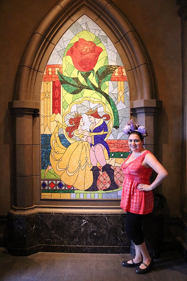 a woman posing next to a tile mosaic of a scene from Beauty and the Beast
