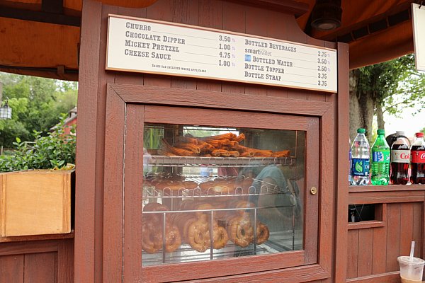 a wooden food cart selling churros and Mickey pretzels with a menu hanging over the top
