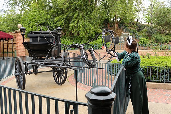 a woman petting an invisible horse in front of a black carriage