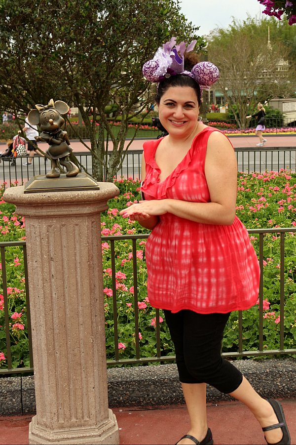 a woman in a red shirt posing next to a statue of Minnie Mouse