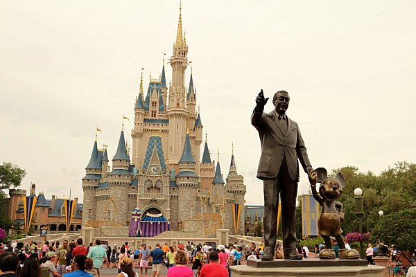 a statue of Walt Disney and Mickey Mouse in front of Cinderella\'s Castle