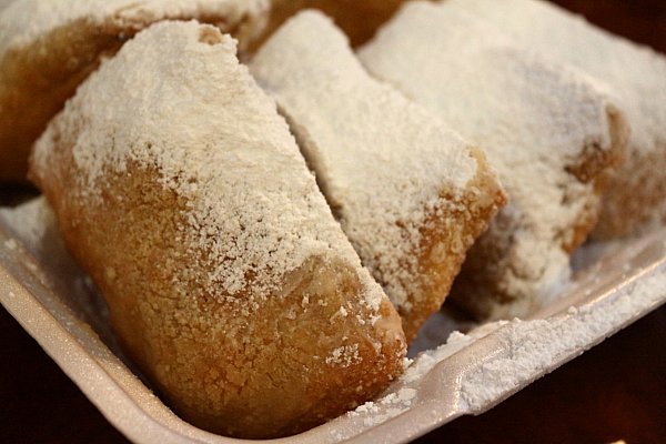 A closeup of fried beignets topped with powdered sugar in a white takeout container