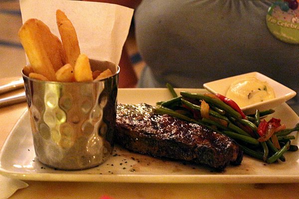 a metal cup of french fries, a cooked steak, and green beans on a white plate