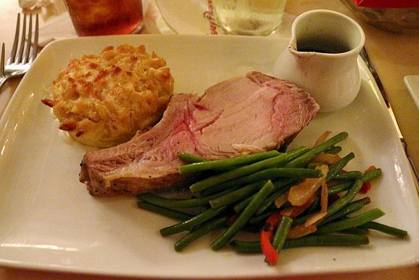 a roasted pork chop with baked macaroni and cheese and green beans on a white plate