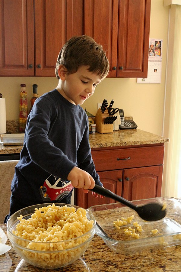 A young boy scooping cooked macaroni into a glass baking dish