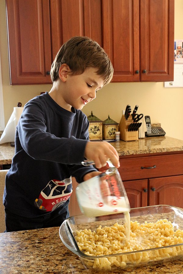 A boy pouring milk out of a measuring cup into a glass baking dish