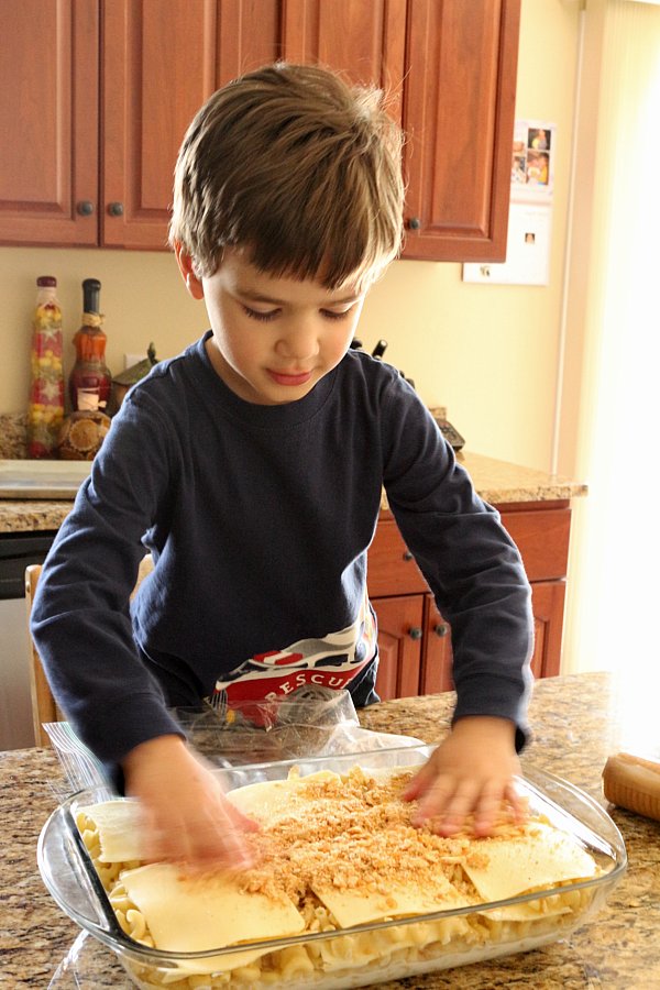 A young boy spreading crushed cracker crumbs over a casserole dish