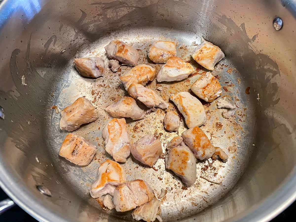 Lightly browned cubes of chicken breast in a metal pot.