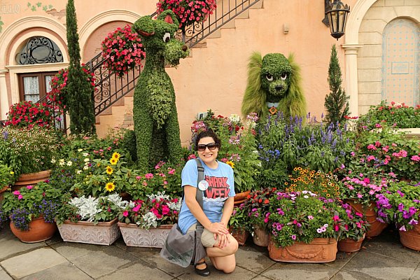 A woman posing in front of a garden with dog shaped topiaries