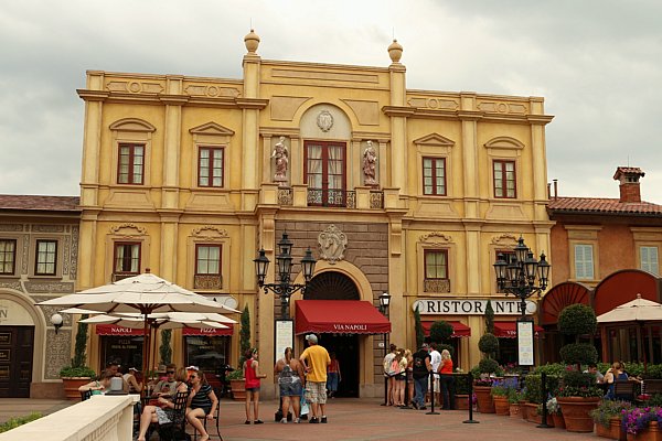 a building with a red awning and tables with white umbrellas in front