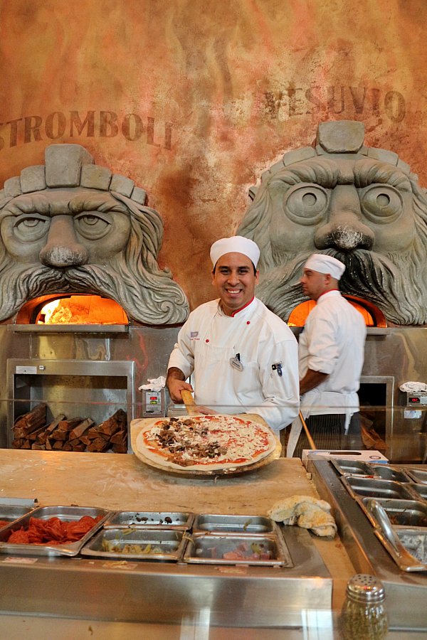 A man posing with a large pizza in a restaurant kitchen