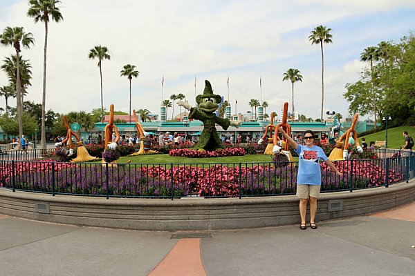 A woman posing in front of a Mickey Mouse topiary with palm trees in the distance