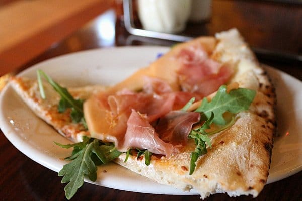 A slice of melon and prosciutto pizza on a white plate