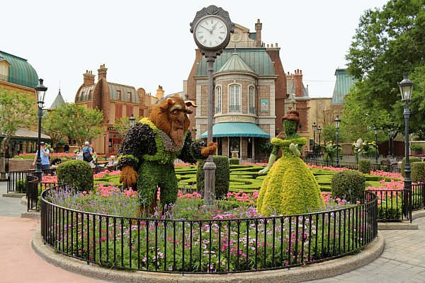 a Beauty and the Beast topiary in front of a clock and French style buildings