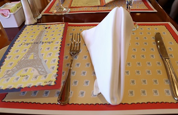 a table setting with a place mat, menu, fork, and cloth napkin