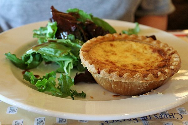 a small round quiche served with salad on a white plate