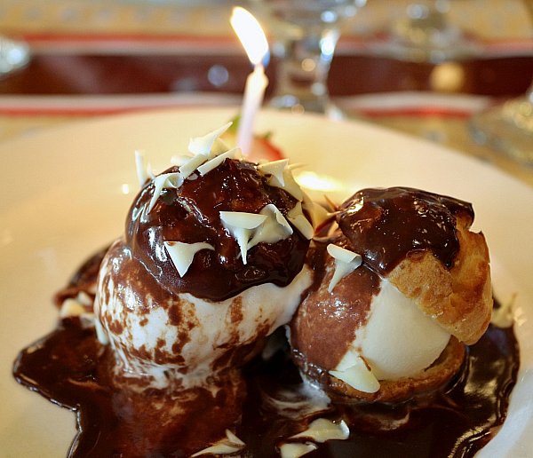 a profiterole dessert filled with ice cream and topped with chocolate sauce on a white plate
