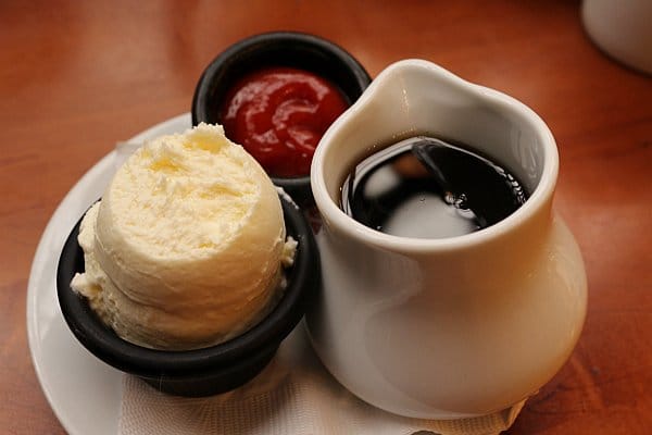 small containers of soft butter, ketchup, and maple syrup on a table