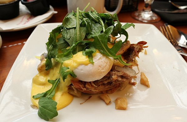 pulled pork topped with poached eggs, Hollandaise sauce, and arugula on a white plate