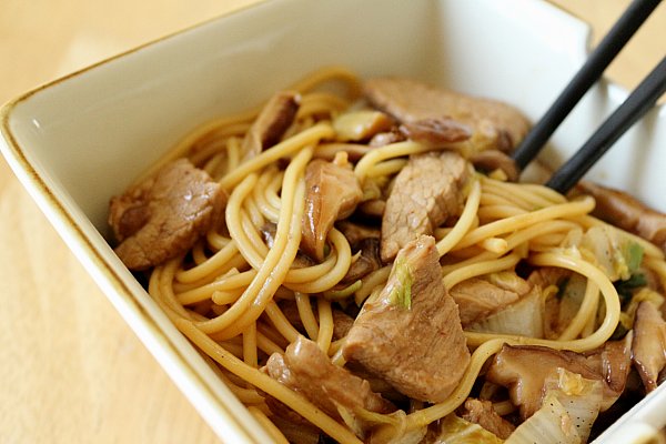 a closeup of pork lo mein noodles in a square bowl with black chopsticks