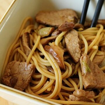 closeup of a square bowl filled with noodles, sliced pork, and mushrooms