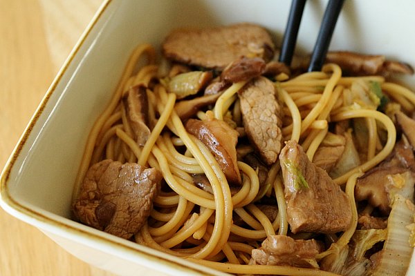 closeup of a square bowl filled with noodles, sliced pork, and mushrooms