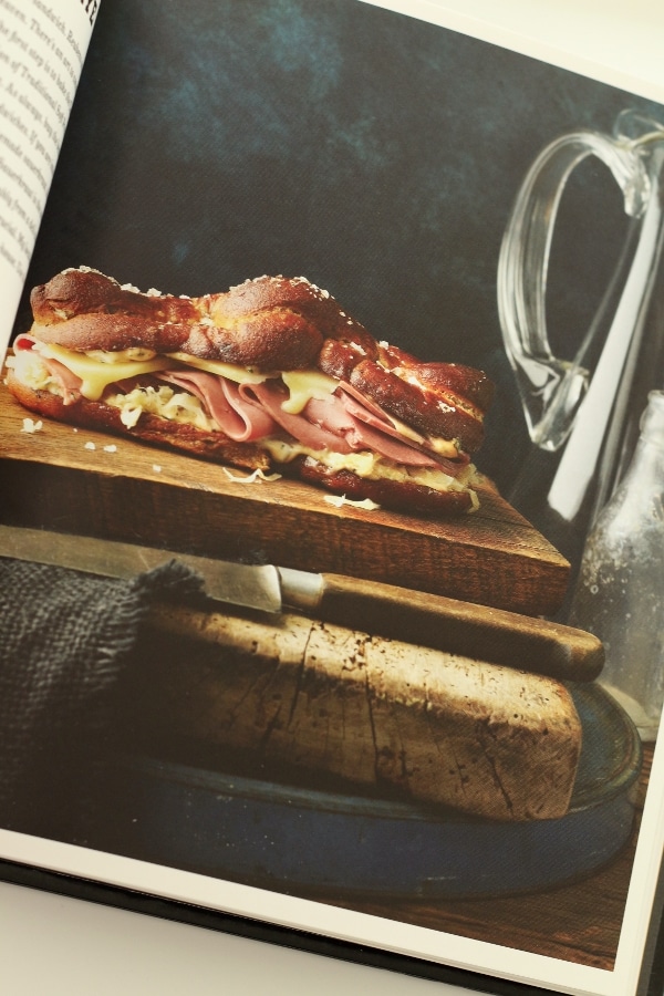 a sandwich made with pretzel bread, cold cuts, and mustard on a wooden board