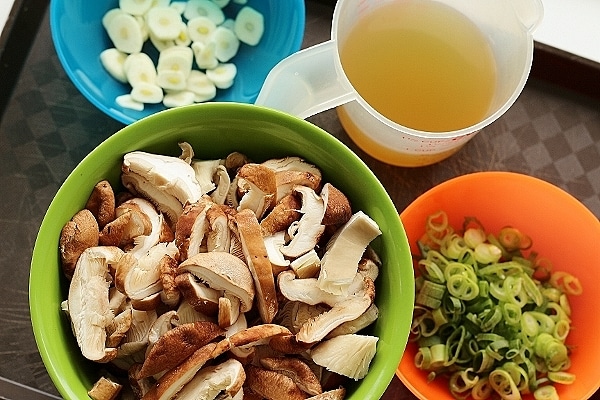 overhead view of colorful containers of ingredients including sliced mushrooms, garlic, and scallions