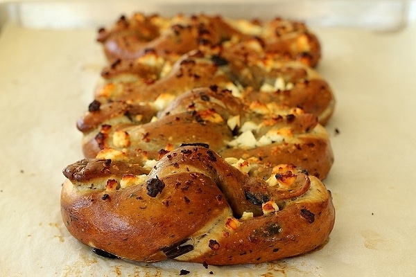 Row of Philadelphia style soft pretzels with olives, garlic, and feta cheese