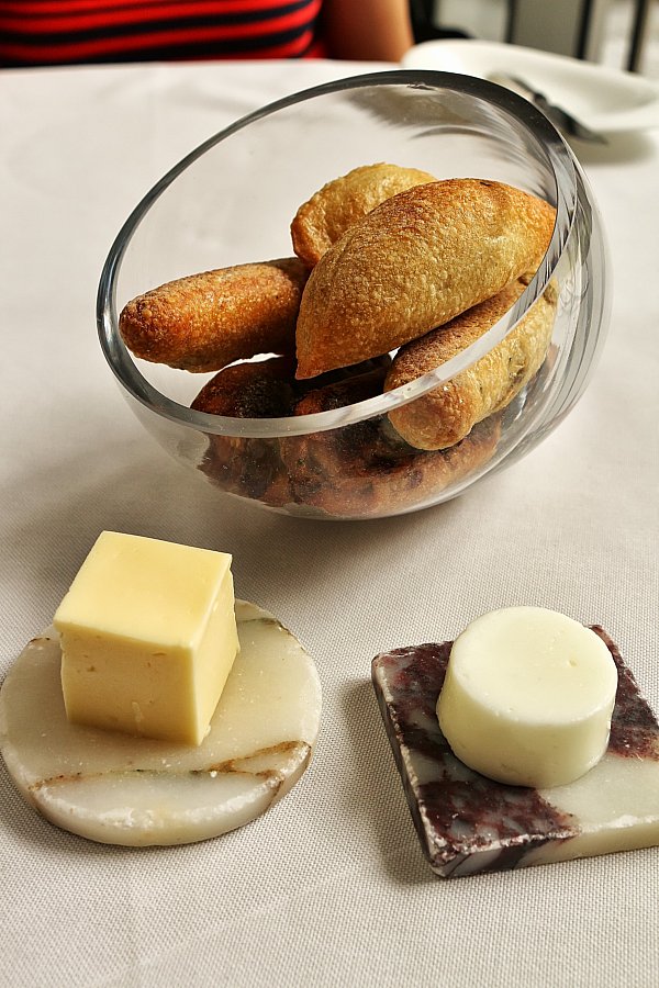 small loaves of bread in a glass bowl with blocks of butter on the side