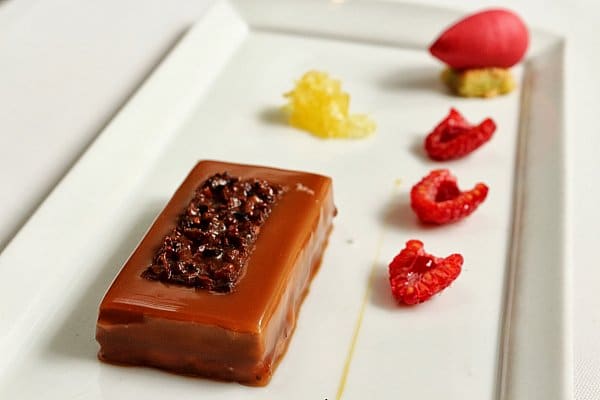 a brown rectangular dessert with raspberry halves on a white plate
