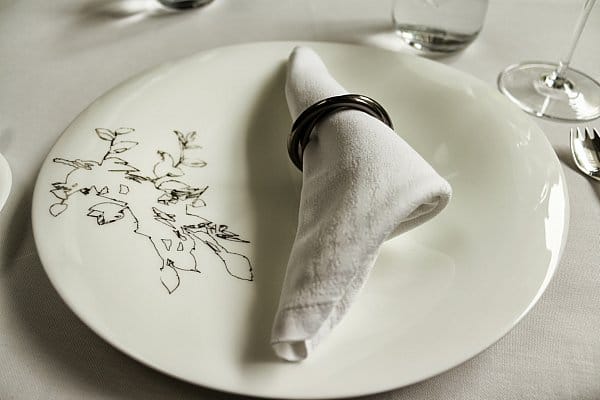 a white plate topped with a white cloth napkin in a metal ring