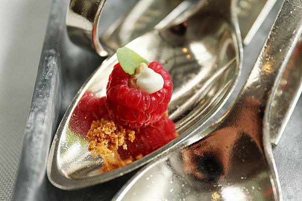 a metal spoon topped with a raspberry filled with white cream