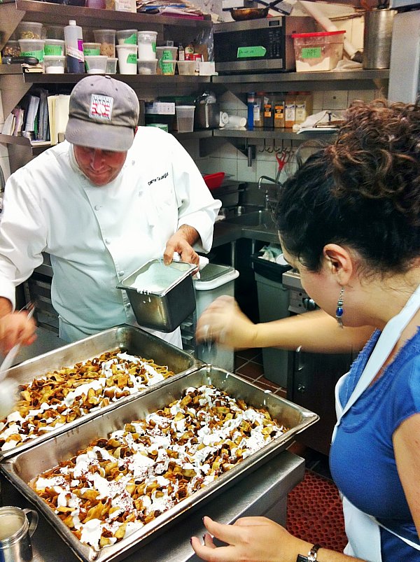 a man and woman garnishing pans of food in a professional kitchen