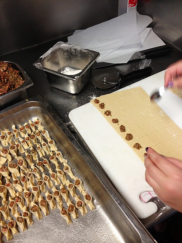 two hands assembling food on a white surface next to a pan of food