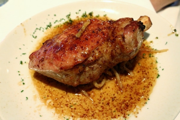 a large seared pork chop on a white plate with light brown sauce
