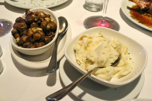 overhead view of bowls of sauteed mushrooms and mashed potatoes on a white surface