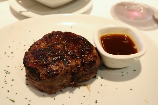 a filet mignon steak on a white plate with a cup of brown sauce on the side