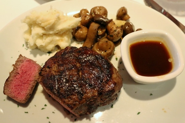 overhead view of a plate of steak, mushrooms, mashed potatoes, and a cup of brown sauce