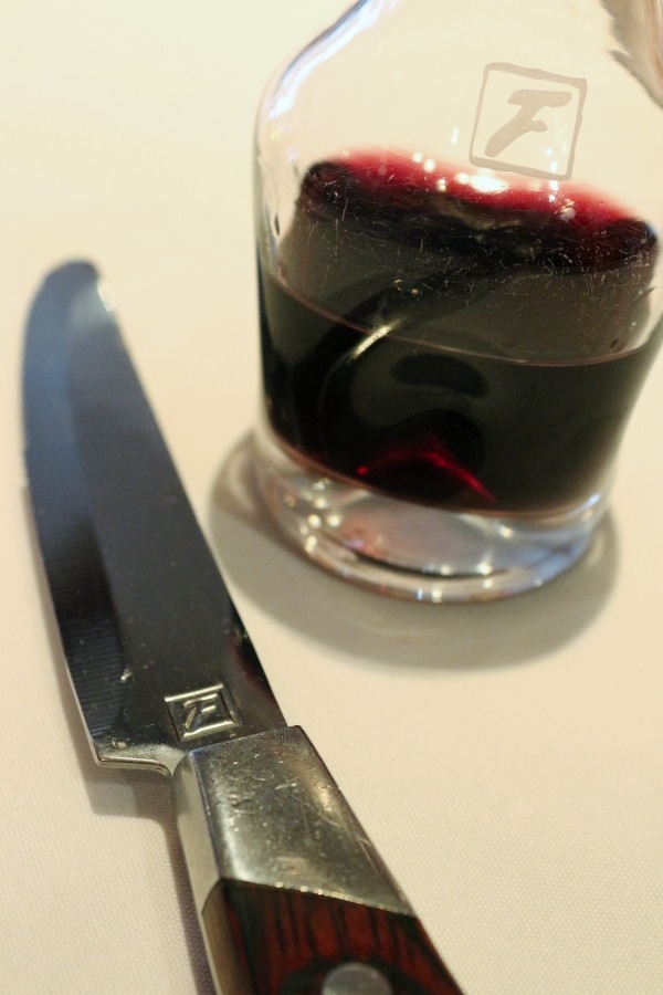 A knife sits next to a glass of wine on a white surface